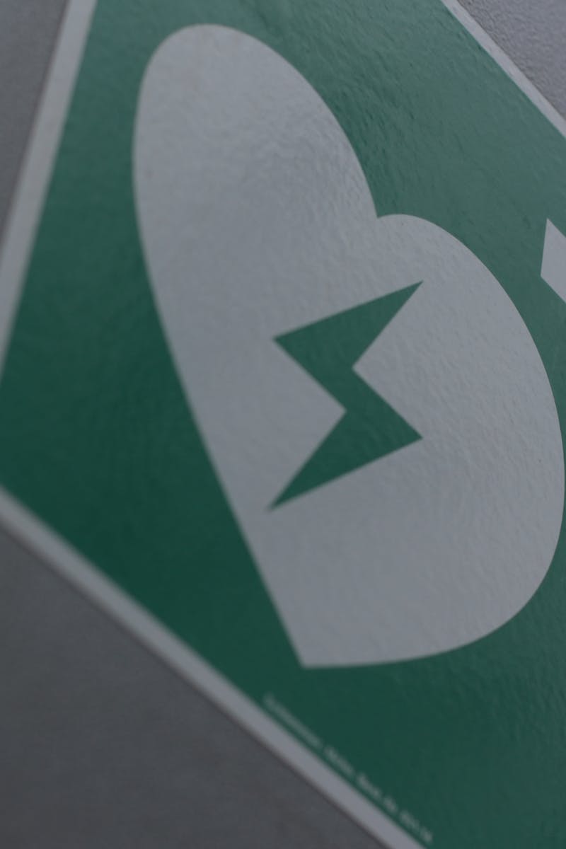Green first aid sign featuring a broken heart and cross symbol for medical emergency awareness.